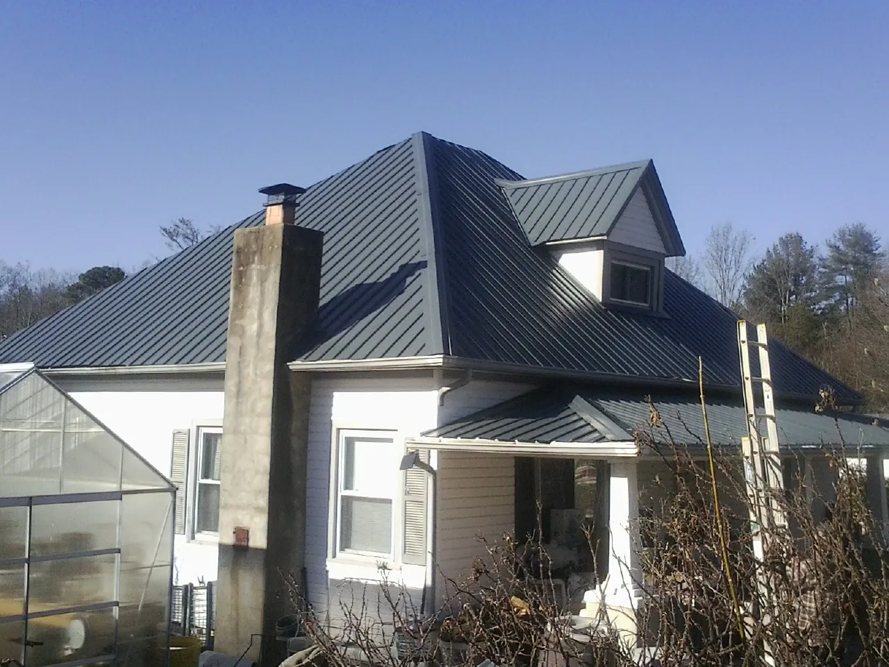 Dark blue standing seam metal roof on a white farmhouse with dormer — Slate & Tile Roof Repair by Roofing Brothers in Watsontown