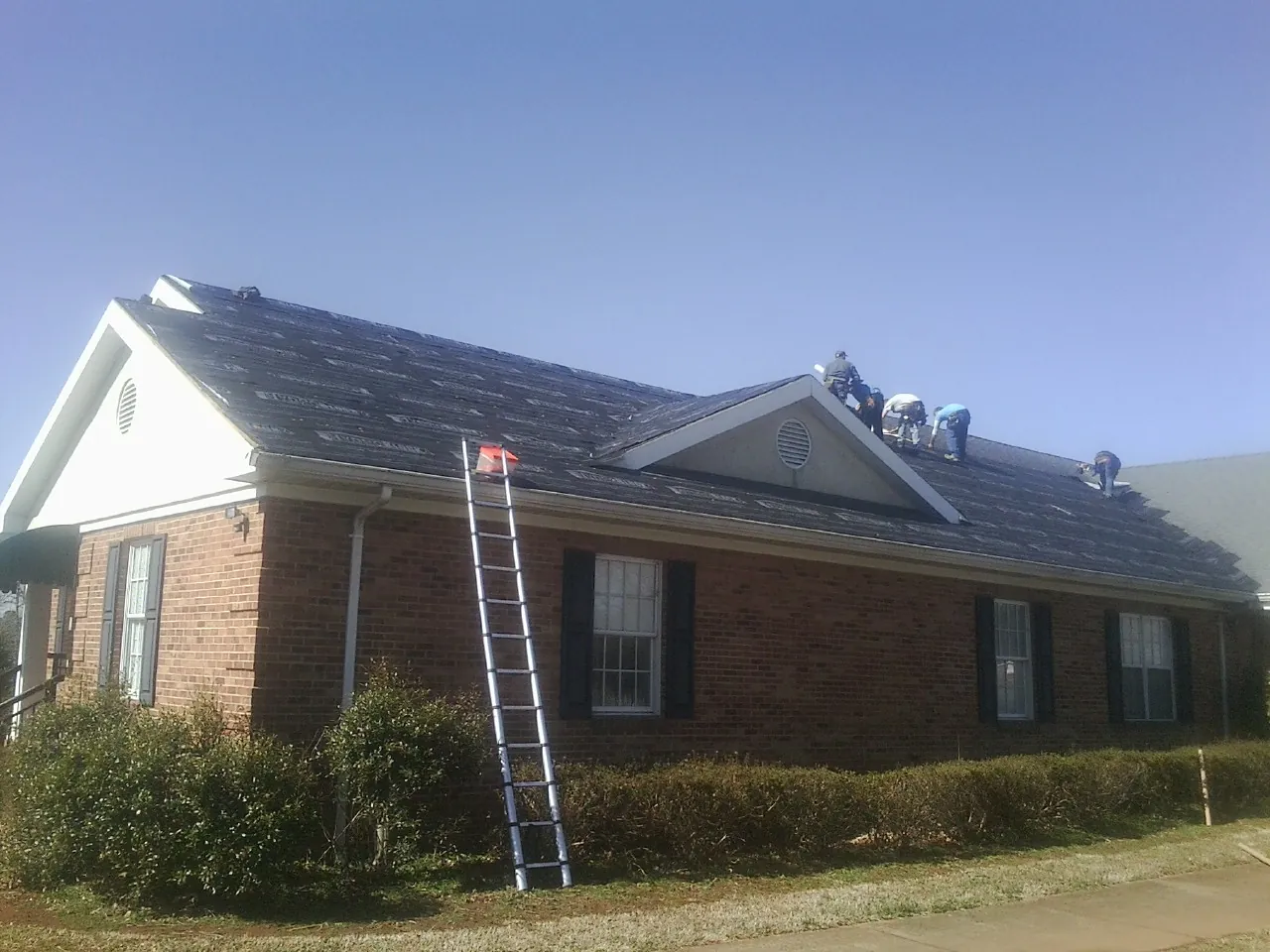 Crew tearing shingles off a brick ranch roof with a ladder set — Metal Roof Repair work by our crew in Watsontown