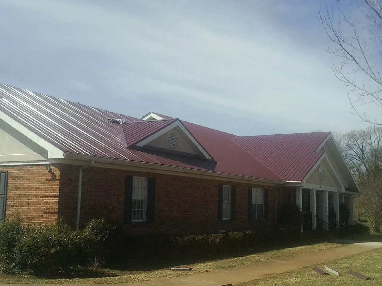 Red metal roof with gabled entries on a long brick building, from a Hail Damage Roof Repair job in Watsontown