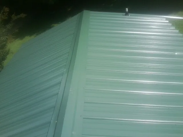 New green metal panels meeting at the ridge of a roof — Flat Roof Repair work by our crew in Watsontown