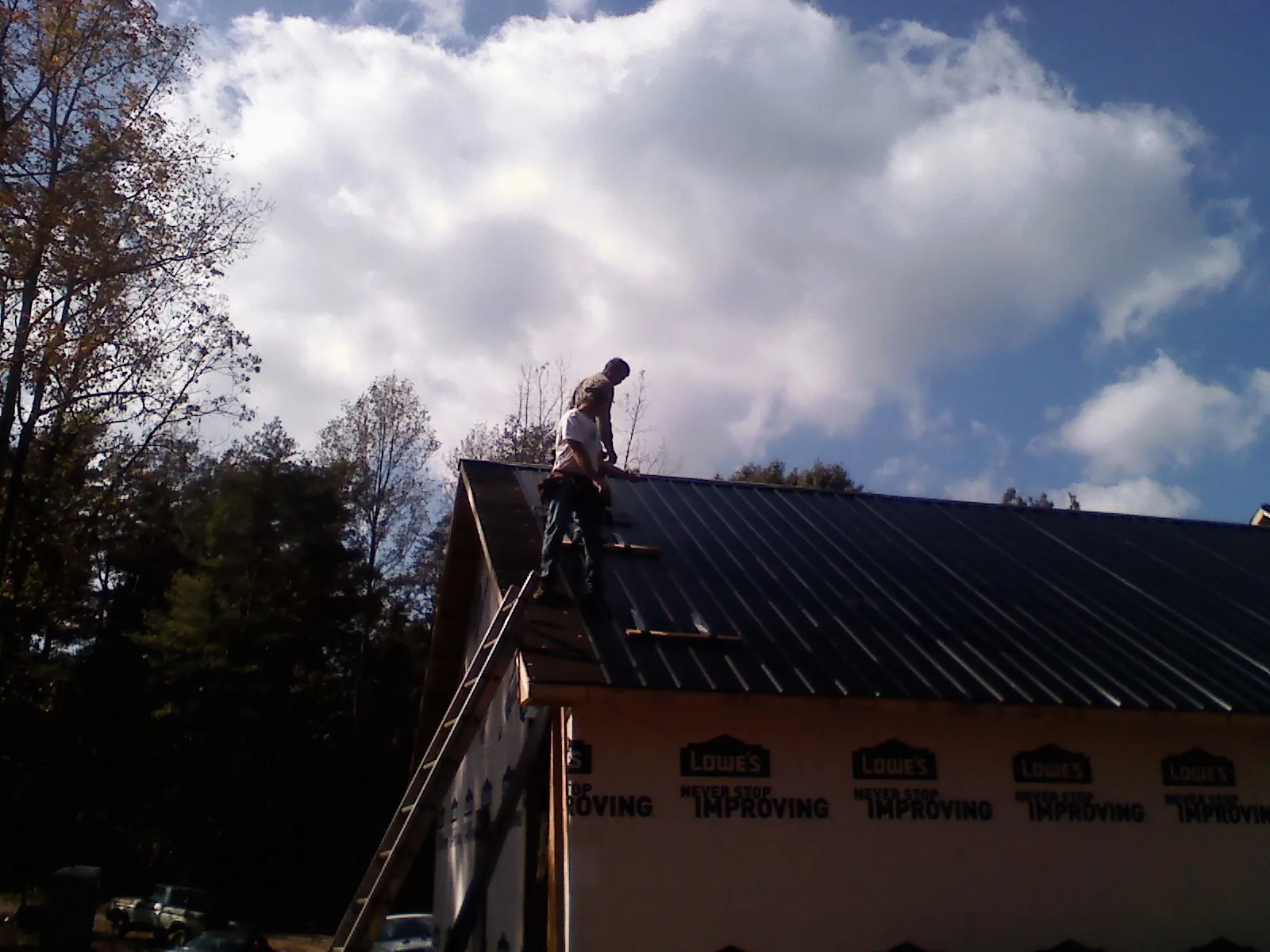 Roofer fastening dark metal panels high against a cloudy sky, from a Roof Inspection job in Watsontown