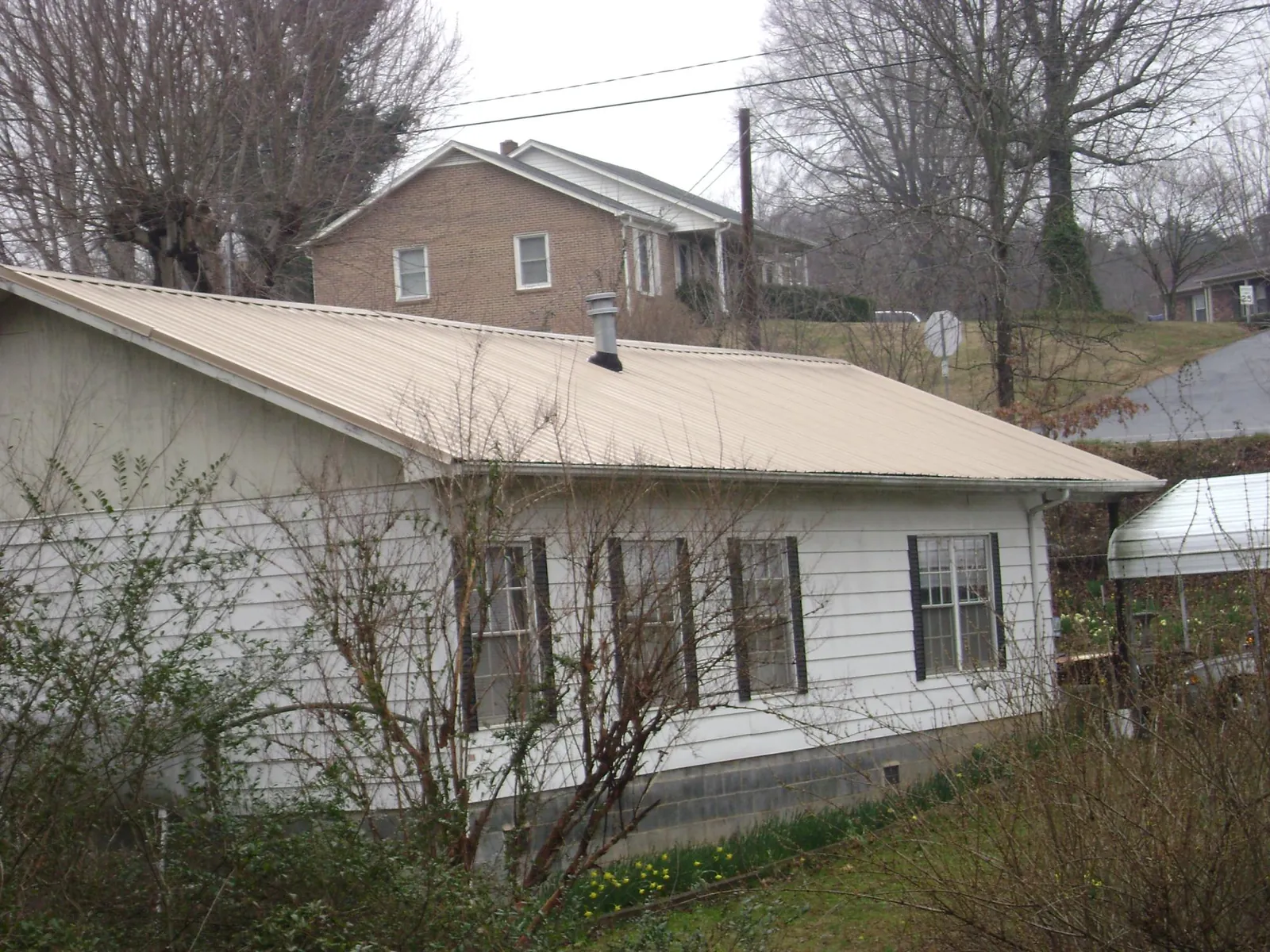 Tan metal roof on a white sided house set into a hillside — Commercial Roofing by Roofing Brothers in Watsontown